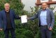 Klaus Bouillon und Christian Precht halten die Urkunde der Sicherheitspartnerschaft jweils in einer Hand, stehend vor dem Rathaus